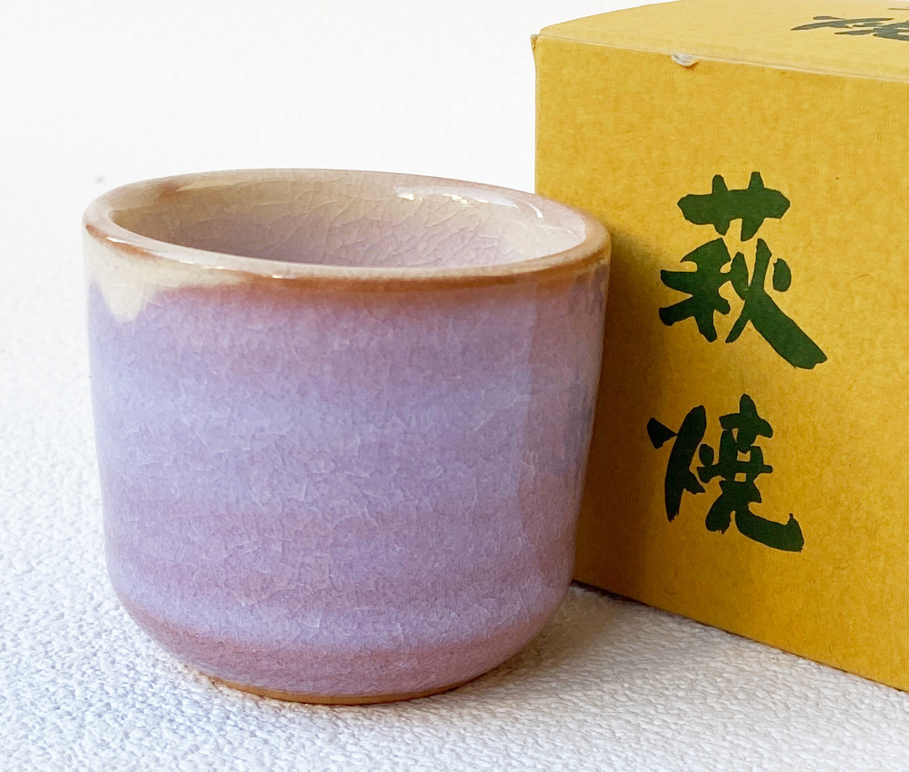 A Hagi-ware guinomi sake cup in a contemporary purple glaze, shown beside its box marked Hagi-yaki