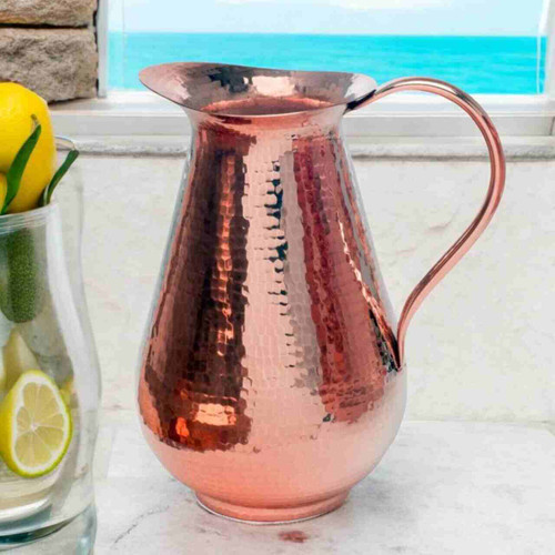 Image shows our elegant Sertodo Bisotun Ayurvedic Copper Water Pitcher, on a stone ledge with.an ocean view. Your perfect hydration.