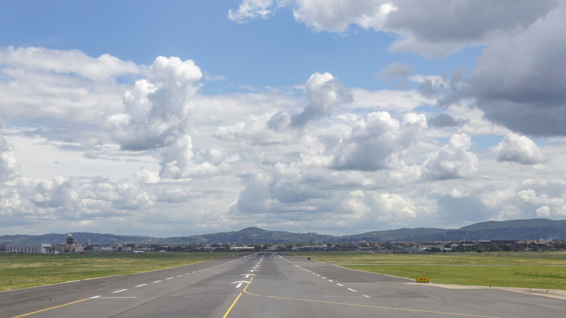 airport runway with mountains in background and sunny sky with white puffy clouds