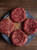 Four beef burgers, prepped and ready to cook on a plate - grass fed beef