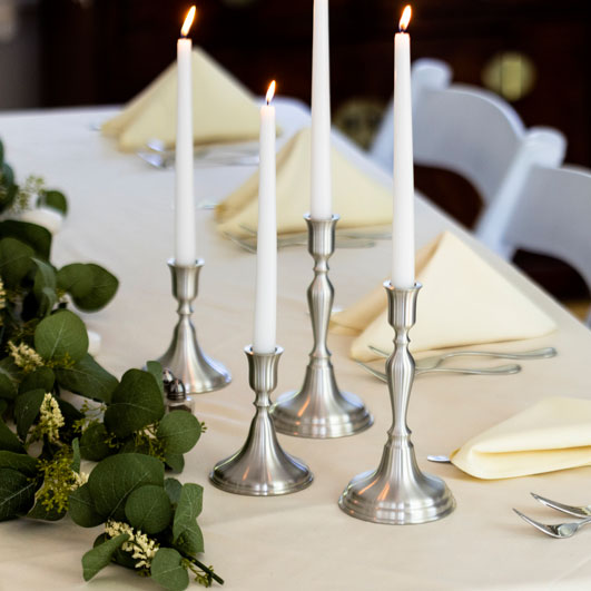 Multiple heights of pewter taper candlesticks set on a wedding table