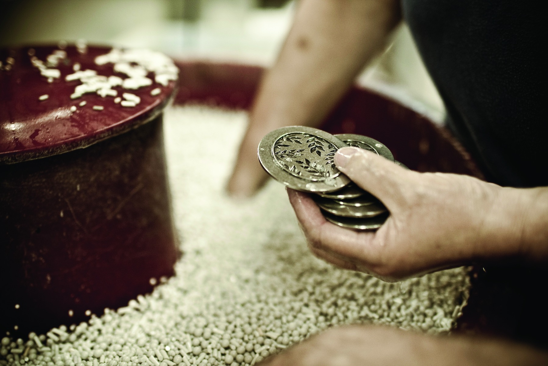 Hands putting pewter in a vat of ceramic tumbling media