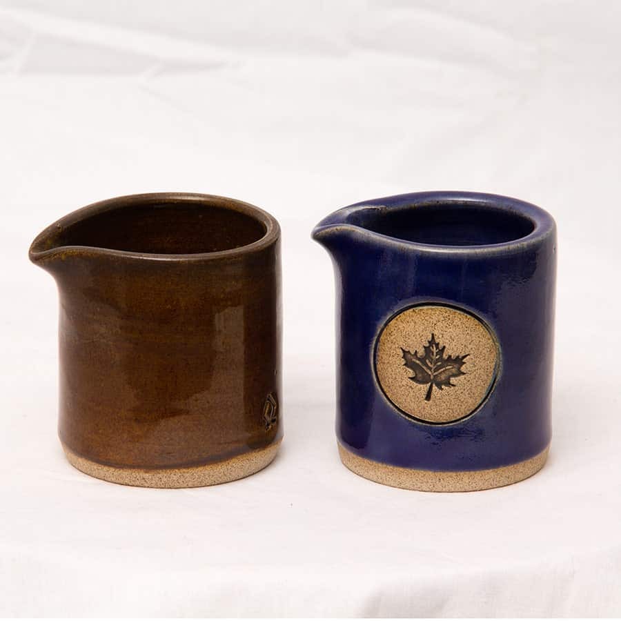 Two tiny pottery pitchers for maple syrup, one in brown and one in blue