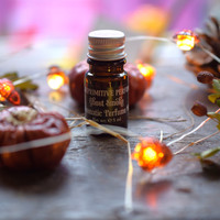 Ghost Smoke Perfume oil sat on a dark wooden stool surrounded by acorn lights and dried pumpkins