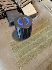 LAPG Tactical Spare Battery Container TDP-RDBATTHOLDER, a cylindrical black storage container with a blue logo on top, placed on a tactical gear mat. Thumbnail Image