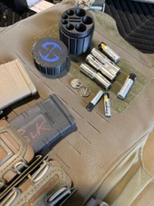 LAPG Tactical Spare Battery Container, TDP-RDBATTHOLDER, black cylindrical battery holder with multiple slots for batteries, placed on a tactical gear surface with batteries and other equipment. Thumbnail Image