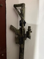 LAPG AR-15 Buffer Tube Wall Mount TDP-ARWM, mounted on a white wall, holding a tactical rifle with a scope and orange accents. Thumbnail Image