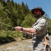 Suunto Core 2 Classic Outdoor Watch, a rugged black wristwatch with digital display, worn by a man fishing outdoors by a river, surrounded by lush green trees. Thumbnail Image