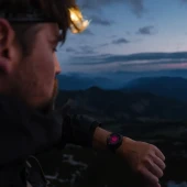Suunto Core 2 Classic Outdoor Watch, a rugged wristwatch with a black rubber strap and digital display, worn by a person hiking during dusk with a mountainous landscape in the background. Thumbnail Image