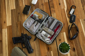Vertx Urban Ghost Utility Pouch VTX5313, open gray tactical pouch with various compartments on wooden table, containing tools, cables, cards, and accessories, alongside gun, sunglasses, keys, wallet, and small potted plant. Thumbnail Image