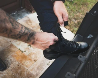 OTB Boots Fusion 8 Black Tactical Boot, a person putting on a black tactical boot with a side zipper, suitable for military or law enforcement use.