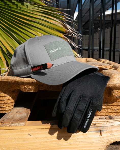Iron & Haft Contractor Anti-Roll Pencil BM-PENCIL 840277209825, gray cap with patch and black glove with logo, outdoor setting with wooden surface and tropical plant leaves.