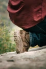 OTB Boots Incline Mid Waterproof Tactical Boot, close-up of a person crouching outdoors wearing tan waterproof tactical boots and dark jeans in a natural setting.