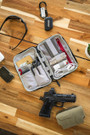 Vertx Urban Ghost Utility Pouch VTX5313, organized inside a gray tactical pouch with elastic straps holding tools and accessories, displayed on a wooden surface with a handgun, sunglasses, and miscellaneous items.