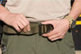 Model putting on 5.11 Tactical 1.75 Operator Belt on green pants