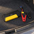 Arrancador ADM negro con panel amarillo junto a su cable de pinzas roja y negra en la moqueta del maletero de un coche