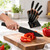 Mano cortando pimiento con el cuchillo de chef negro de virola cobre; detrás, el taco negro con cuatro cuchillos