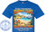 The image is a digitally designed t-shirt mock-up. The t-shirt is a solid, vibrant blue color. Centered on the shirt is a graphic promoting a "15 Day Transatlantic Journeys Cruise."

The graphic depicts a beach scene. In the background, a detailed depiction of a coastal city with buildings and towers is visible. Palm trees frame the sides of the beach scene. A large cruise ship is positioned on the water. In the foreground, there's a sandy beach with two beach chairs, one blue and white striped and the other red and yellow, under a yellow and white striped umbrella. There's a sandcastle, a beach ball, and various beach-related items like sandals and a small bucket. Colorful flowers and foliage are present at the bottom corners of the beach scene.

Above the beach scene, the words "15 Day Transatlantic" are written in white font with a yellow and orange gradient. The words "JOURNEYS CRUISE" are written in a large, bold font with a similar color gradient and a red outline. Beneath the beach scene, the phrase "SAILING ON THE LEGEND" is written in the same bold, gradient font. Below this, the destinations of the cruise are listed: "Civitavecchia (Rome) - Cartagena - Málaga, Gibraltar - Bermuda - Tampa". The date "November 1-16, 2026" is also included. The text "Name Here" is written above the sand, with a space to write a person's name.