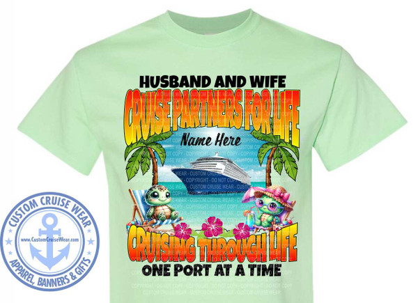The image is a mint green t-shirt with a graphic design printed on the front. The design includes the text "HUSBAND AND WIFE CRUISE PARTNERS FOR LIFE" in a bold, colorful font. Below this, there's a space labeled "Name Here," suggesting where a personal name can be added. The graphic also features a cruise ship sailing on blue water, topped by two palm trees and two turtles on lounge chairs with a drink. At the bottom, the phrase "CRUISING THROUGH LIFE ONE PORT AT A TIME" is displayed. The t-shirt is likely intended for couples who enjoy cruising together. 