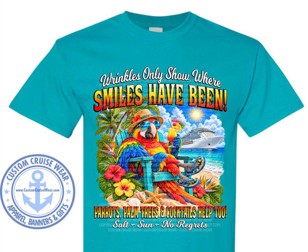 The image displays a teal t-shirt with a vibrant graphic design centered on the chest. The design depicts a tropical beach scene. In the foreground, a brightly colored parrot, predominantly red, blue, and yellow, is seated in a blue Adirondack chair. The parrot wears sunglasses and a straw hat, and holds a cocktail with a straw and an umbrella in one wing, while resting the other wing on its lap. Its feet are clad in flip-flops decorated with palm leaves. The parrot is surrounded by tropical foliage, including palm trees and bright red and yellow hibiscus flowers, along with a starfish and shells on the sandy beach.

In the background, a large white cruise ship is visible on the sparkling blue ocean. The sun shines brightly in the sky, which is filled with fluffy white clouds. The overall scene evokes a sense of relaxation and vacation.

Above the main illustration, a curved text reads "Wrinkles Only Show Where" in a white, elegant script font. Below this, the words "SMILES HAVE BEEN!" are emblazoned in large, bold, multi-colored letters, transitioning from yellow to orange and red, with a black outline. At the bottom of the graphic, another line of text says "PARROTS, PALM TREES & COCKTAILS HELP TOO!" in a similar bold, outlined style. Beneath this, in a cursive script, are the words "Salt - Sun - No Regrets".

On the left side of the t-shirt, below the main graphic, is a circular logo for "CUSTOM CRUISE WEAR". The logo features an anchor symbol in the center within a blue circle, with text around the perimeter and a web address displayed on a banner below the anchor. The t-shirt itself is a solid teal color. The graphic is detailed and colorful, designed to be eye-catching and convey a fun, vacation-themed message.