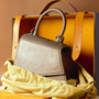 Grey leather handbag displayed with shoulder strap and presentation box