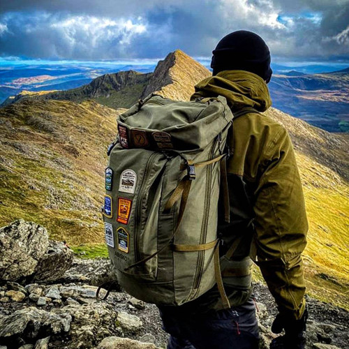 Person walking away from the camera in hills showing 9 patches on their backpack
