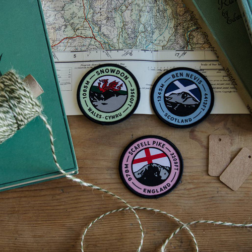 Wood table on which is laid a map, boxes and twine with 3 x UK National Three Peaks patches Ben Nevis, Snowdon and Scafell Pike in the centre