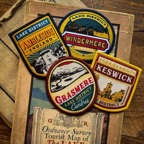 Wood table with folded map and 4 x badges from The Adventure Patch Company scattered over the top