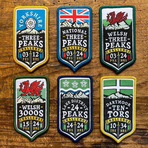 Wood table on which is displayed 6 x Challenge badges from The Adventure Patch Company in 2 lines of 3 patches