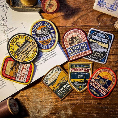 Open book with a stack of national trail patches on a desk from The Adventure Patch Company