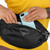 Person in a yellow top wearing the The Osprey Daylite Waist Pack placing a smartphone in the scratch-free glasses & electronics pocket