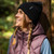 Black Pitted Beanie Hat by Outdoor Research worn by a person leaning against a tree trunk smiling and looking up to the left in woodland