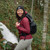 Person outdoors in a red top and black rucksack smiling and facing front wearing a black Juneau Beanie Hat by Outdoor Research
