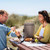 Two people at a picnic table, one is opening a bottle the Greenfield Collection Contemporary Wine Cooler Bag is sat upright on the table