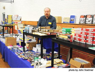 man standing behind table with model railroad books and parts