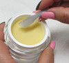 A hand holding a mini cosmetic spatula reaching into a jar of skincare