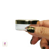 A hand holding a clear cosmetic jar showing the side view of the gold lid