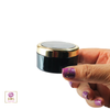 A hand holding a luxury 30 ml black cosmetic jar with a gold rim cap screwed onto the jar base