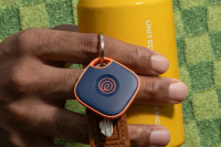 A person holding a yellow can, and a set of keys with a Life360 Tile - Navy Blaze attached to it.