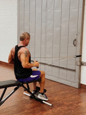 Man doing back exercise with intense resistance band holding intense resistance bands handle grips on intense band adjustable exercise bench with heavy duty  door anchor