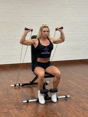 woman doing shoulders exercise with intense resistance band holding intense resistance bands handle grips on intense band adjustable exercise bench