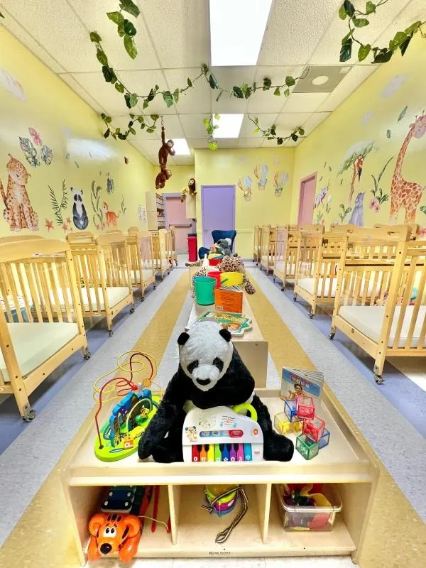 Infant classroom at Kiddie Corner Academy with wooden cribs and animal murals