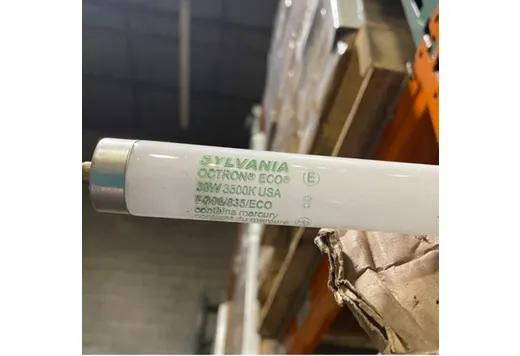 Halco Fluorescent F96 T8 Tube 96in 59W 3500K Single Pin Base Instant Start Dimmable 5900 Lumens Avg Life 18000 hrs, close-up of the fluorescent tube with green markings, stored in a warehouse setting.