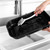 Hand washing a large black roasting tray in a kitchen sink with a cleaning brush