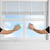 Two hands cleaning a window with cloths beneath white venetian blinds