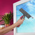 Hand using window cleaning spray and squeegee on glass, with houseplants nearby.