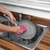 Grey cleaning pad scrubbing white tiled wall near kitchen tap