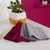 Set of three microfibre cloths in burgundy, pink and grey on a white surface