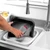Person cleaning roasting tray with pink handle scrubber at kitchen sink