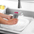 Hands washing a wine glass with a grey silicone dish brush in a white sink